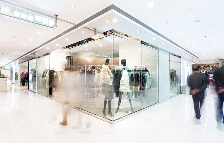 People walking past a clothing store with large glass windows in a shopping mall